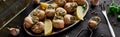 Delicious cooked escargots with lemon slices on black wooden table with spices and white wine, panoramic shot.