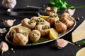 Delicious cooked escargots with lemon slices on black wooden table.
