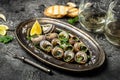 Delicious cooked sea escargo snails with herbs, butter, garlic on metal plate with forks. wine glass. gourmet food. Restaurant Royalty Free Stock Photo