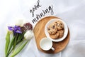 Delicious cookies, flowers and GOOD MORNING wish on white cloth, flat lay