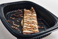 Delicious crepe adorned with chocolate and caramel drizzle in a black takeout container Royalty Free Stock Photo