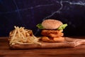 Delicious crispy fish burger with fried potatoes on wooden table. Royalty Free Stock Photo