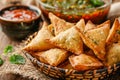 Delicious Crispy Golden Brown Samosas in Basket with Sauces and Fresh Herbs on Rustic Wooden Table
