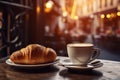 Delicious croissant and cup of coffee on wooden table, cafe in the background