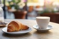 Delicious croissant and cup of coffee on wooden table, cafe in the background