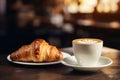 Delicious croissant and cup of coffee on wooden table, cafe in the background