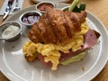 Delicious croissant sandwich with ham, cheese and scrambled eggs on plate served at cafe restaurant Royalty Free Stock Photo