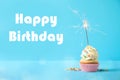 Delicious cupcake with sparkler on blue background. Happy Birthday