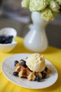 Delicious dessert at home. A big Belgian waffle with a scoop of vanilla ice-cream and organic blueberries on a white plate on a ye Royalty Free Stock Photo