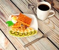 Delicious dessert, Viennese waffles with ice cream and kiwi and banana slices on a wooden table next to a coffee mug Royalty Free Stock Photo