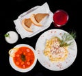 Delicious dinner table with Fettuccine pasta with meat, hot soup with sausages, bread and compote on isolated black background