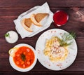 Delicious dinner table with Fettuccine pasta with meat, hot soup with sausages, bread and compote on wooden background.