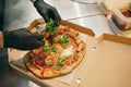 Delicious dish. Chef puts arugula on hot baked pizza in cardboard box. Looks tasty, aromatic Royalty Free Stock Photo