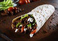 Delicious doner kebab shawarma roll showcased on a wooden board. Warm pita enveloping succulent chicken and fresh vegetables,