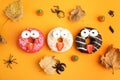 Delicious donuts decorated as monsters on orange background, flat lay. Halloween treat