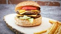 Delicious double tasty hamburger with beef cutlet, french fries, fresh vegetables and  2 slices of cheddar cheese on vintage woode Royalty Free Stock Photo