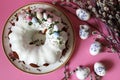A delicious Easter cake - a ring in white icing on a pink table background next to willow branches and Easter eggs. Royalty Free Stock Photo