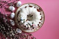 A delicious Easter cake - a ring in white icing on a pink table background next to willow branches and Easter eggs. Royalty Free Stock Photo