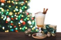 Delicious eggnog in glass, gift box, festive ornaments on wooden table against Christmas tree, space for text