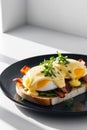 Delicious eggs benedict with bacon and herbs served on toasted bread on a black plate. Royalty Free Stock Photo
