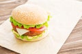 Delicious fast food. Cheese burger with grilled meat, cheese, tomato, on craft paper on wooden surface. Fast food Royalty Free Stock Photo