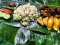 A Nasi Liwet on a Banana Leaf with a Fried Chicken, Tomato, Some Spicy Sambal, Cucumber, Green Peas, tempeh, and tofu