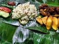 A Nasi Liwet on a Banana Leaf with a Fried Chicken, Tomato, Some Spicy Sambal, Cucumber, Green Peas, tempeh, and tofu