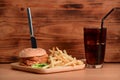 Fish burger with fried potatoes and soft drink on wooden table. Royalty Free Stock Photo