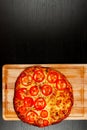 Delicious fragrant hot pizza on a wooden cutting board on a black table
