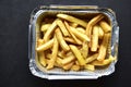 Delicious French fries in an aluminum container on a black background