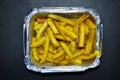 Delicious French fries in an aluminum container on a black background