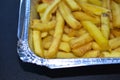 Delicious French fries in an aluminum container on a black background