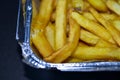 Delicious French fries in an aluminum container on a black background