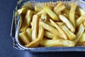 Delicious French fries in an aluminum container on a black background