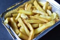 Delicious French fries in an aluminum container on a black background