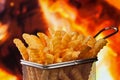 Delicious french fries in frying basket serving recipient on fire background