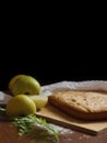 Delicious fresh baked goods lie on a wooden board along with fresh pears and lemon on a dark wooden table on a black