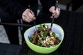 Delicious fresh healthy salad in a green bowl mixed by a woman hands with salad spoon food