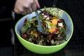 Delicious fresh healthy salad in a green bowl mixed by a woman hands with salad spoon food Royalty Free Stock Photo