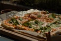 Delicious fresh home made pizza served on a wooden board and some paper. Tasty pizza ready to be cut