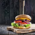 Delicious fresh homemade burger with cheese, tomatoes, salad and onions on a wooden table, close up Royalty Free Stock Photo