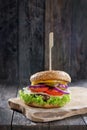 Delicious fresh homemade burger with cheese, tomatoes, salad and onions on a wooden table, close up Royalty Free Stock Photo