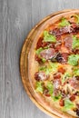 Delicious fresh italian pizza with ham, salami, tomatoes, salad and parmesan on a wooden board on a wooden table. Top Royalty Free Stock Photo