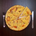 Delicious fresh cheese pizza with ham, sausage, tomatoes on black table, on white plate, fork, knife nearby, top view Royalty Free Stock Photo