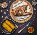 Delicious fried chicken with rice on a cutting board, fork for meat, spicy sauce, spices, garlic and corn in the pan on dark blue