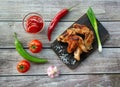 Delicious fried chicken wings. Tomatoes, sauce, hot peppers, garlic and onion on a wooden background. Top view Royalty Free Stock Photo