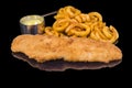 Delicious fried crispy fish fillet with panko garnished with sauce and fried onion rings with reflection