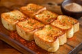 Delicious Golden Brown Garlic Bread Slices Sprinkled with Herbs Served on a Wooden Board with Dip