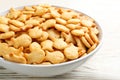 Delicious goldfish crackers in bowl on wooden table, closeup