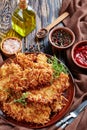 Delicious grated potato breaded pork chops on a clay plate on a rustic wooden table with tomato sauce in a bowl, vertical view